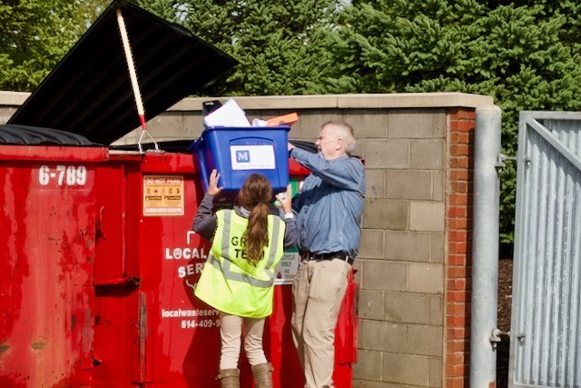 student and teacher emptying trash into dumpster